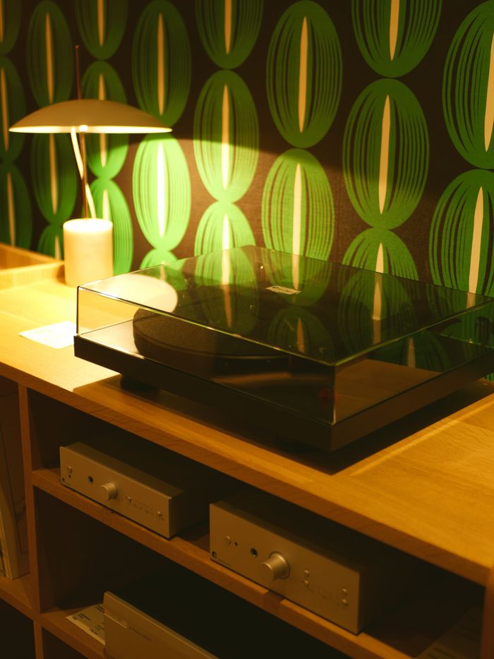 delivery-policy A chic vinyl turntable setup on a modern wooden shelf with a stylish green patterned wallpaper backdrop.