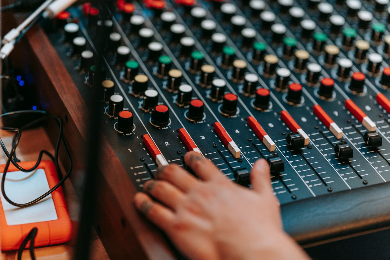 Close-up of a hand adjusting controls on a professional sound mixer in a recording studio.